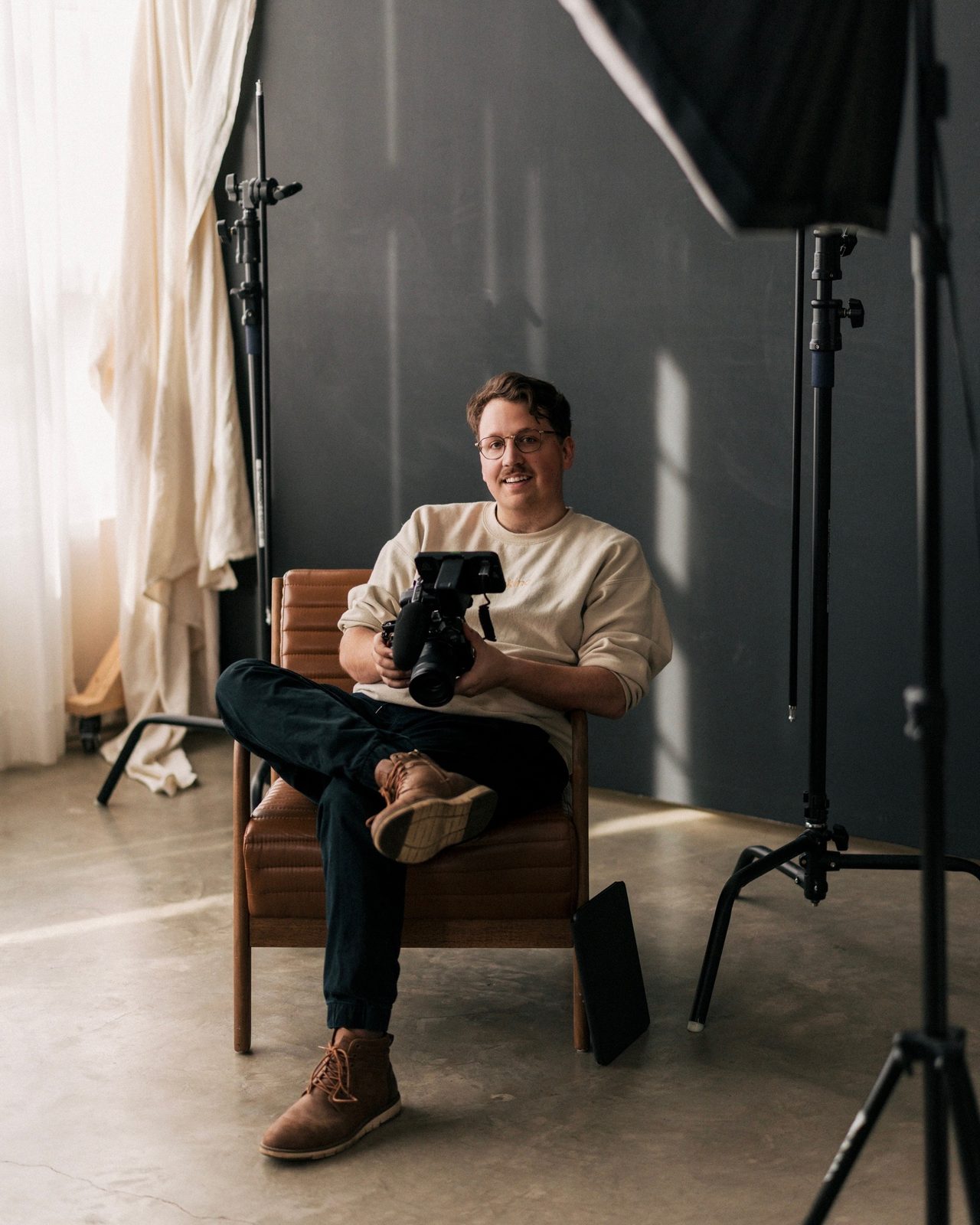 Jacob Clark seated in his studio with a camera in his hands, softbox light to one side.