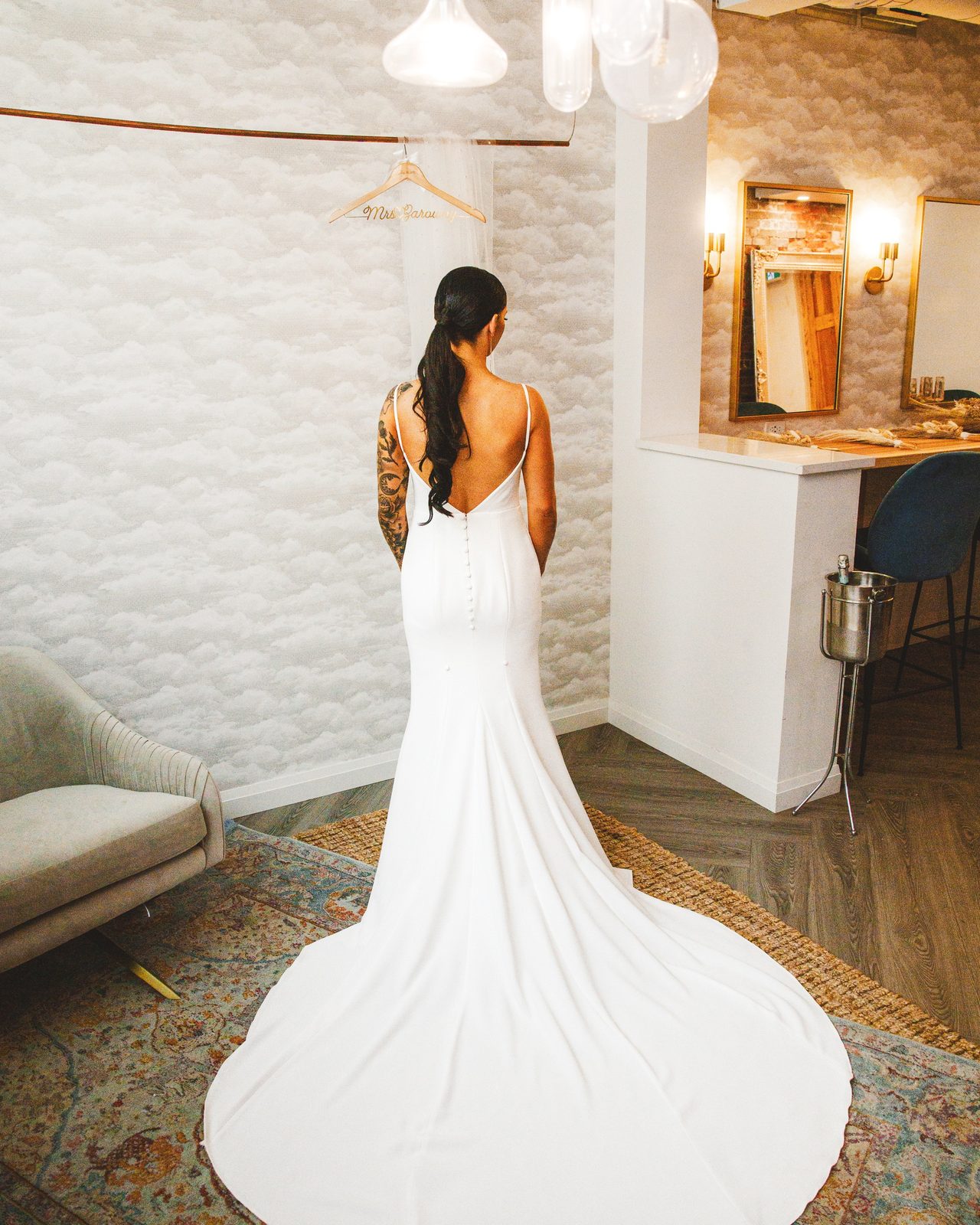 A bride in an open-back gown with a long train, in the room where she got ready.