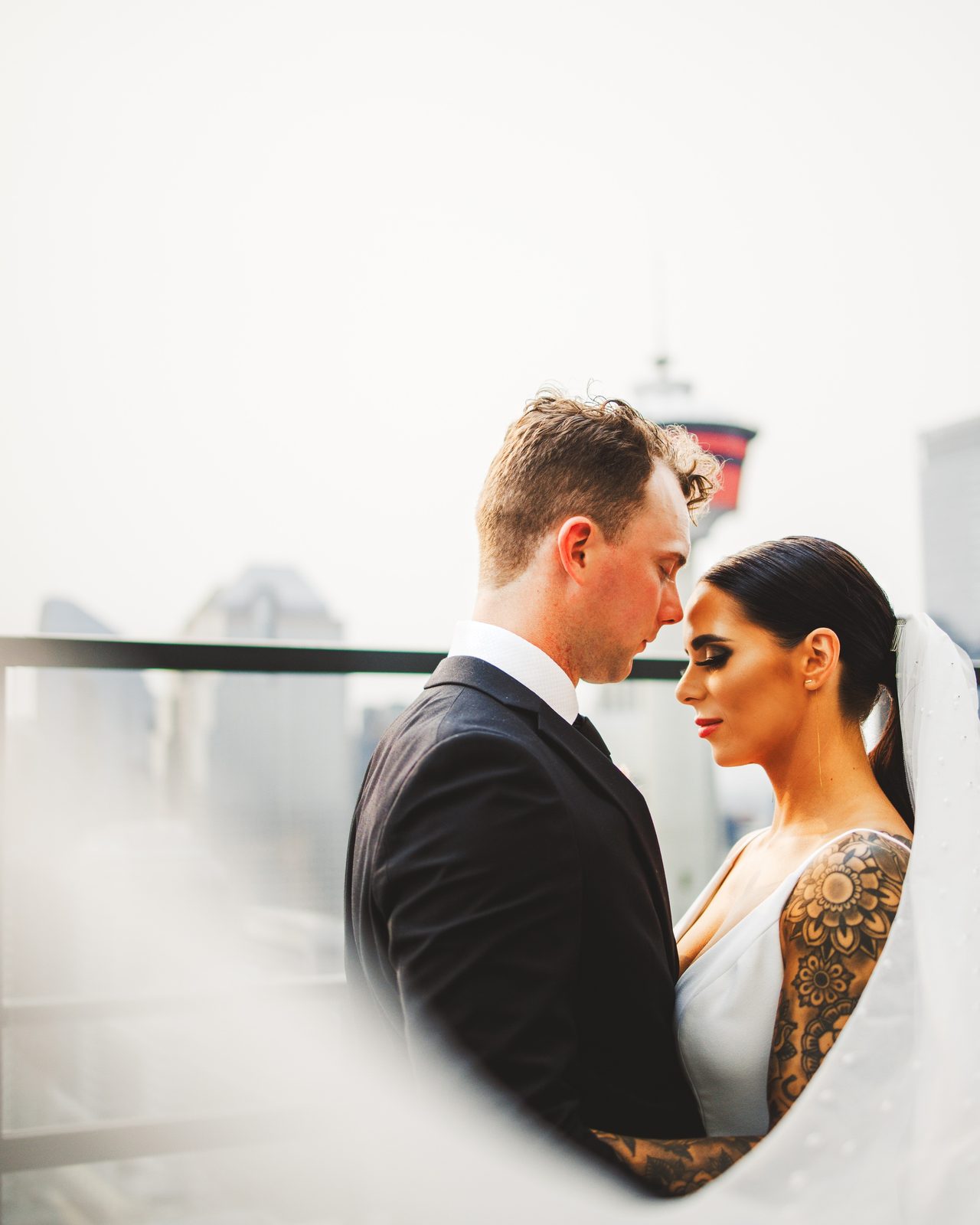 A couple stand close together, a veil drifting across the frame.