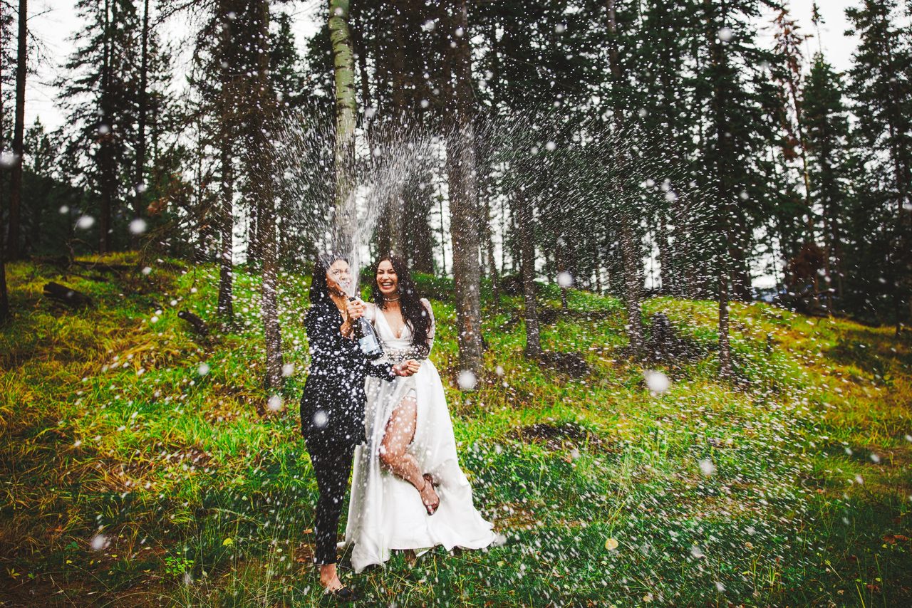 A bride laughs as confetti falls around her in a sunlit forest clearing.