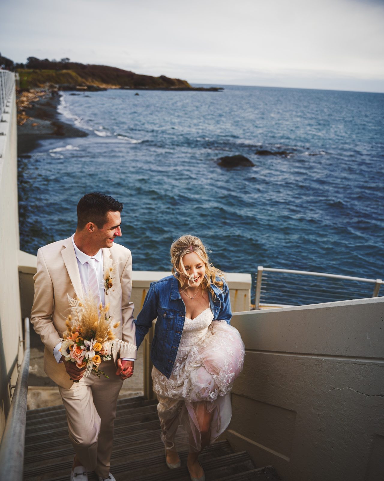 A couple hurry down a flight of steps, the sea behind them.
