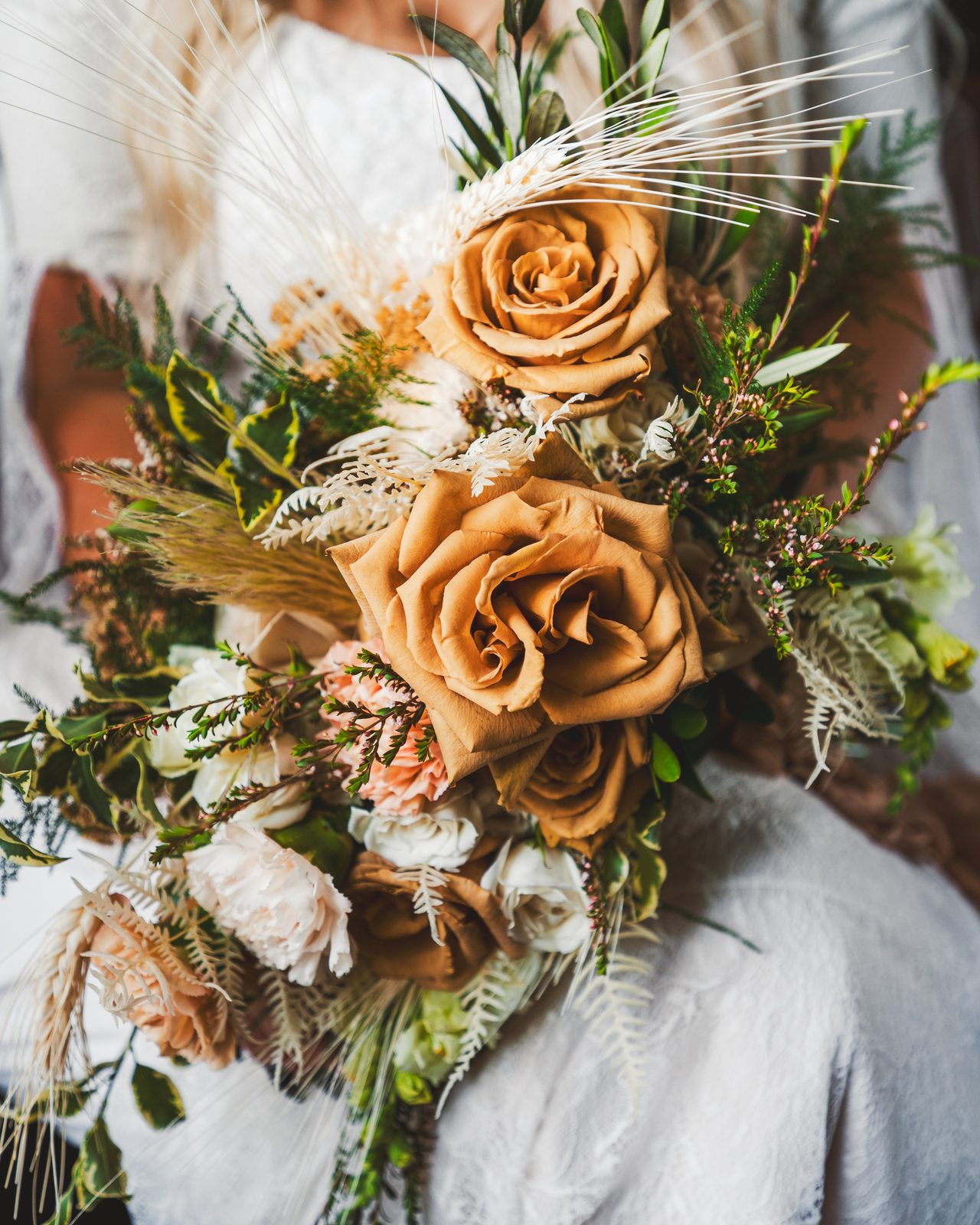 A bouquet of caramel roses and dried grasses, held close.