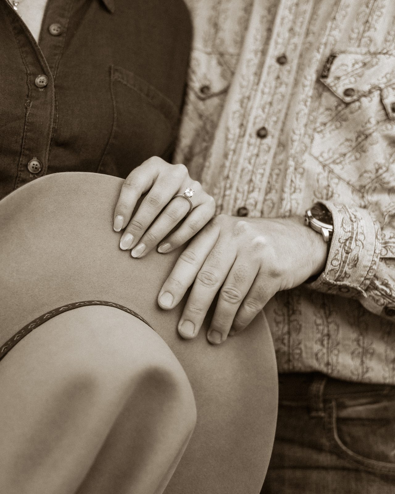 A couple's hands rest together on a felt hat.